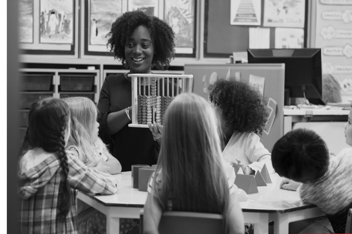 A child care worker reads to young children who follow along in the book she holds.